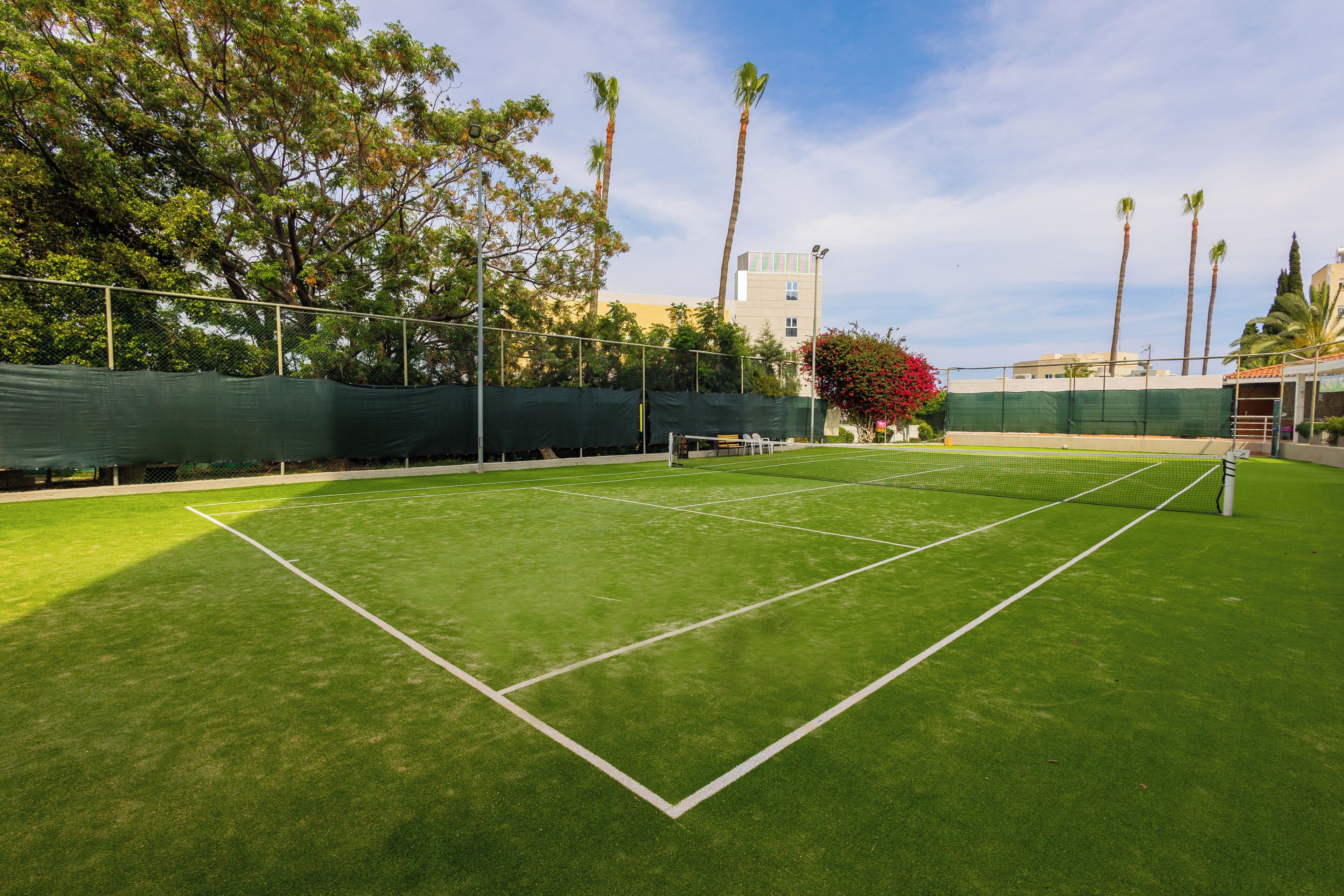 A tennis court with a net, surrounded by trees and a building in the background.