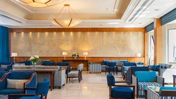Un hall d’hôtel avec des sièges recouverts d’un tissu bleu, un comptoir d’accueil en bois et une grande fresque murale.