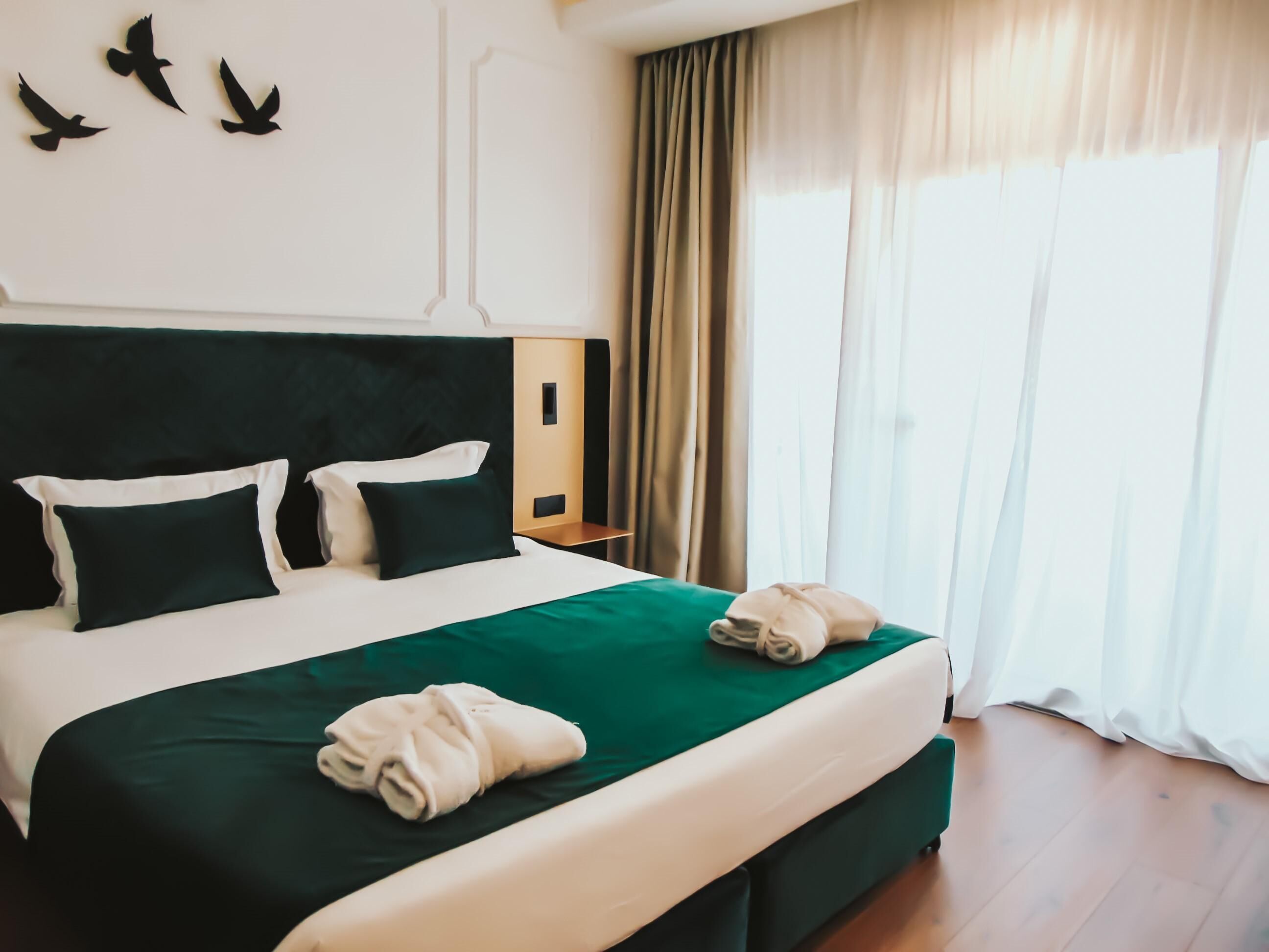 Una cama bien hecha con una colcha verde, dos almohadas y una toalla doblada en el reposapiés.