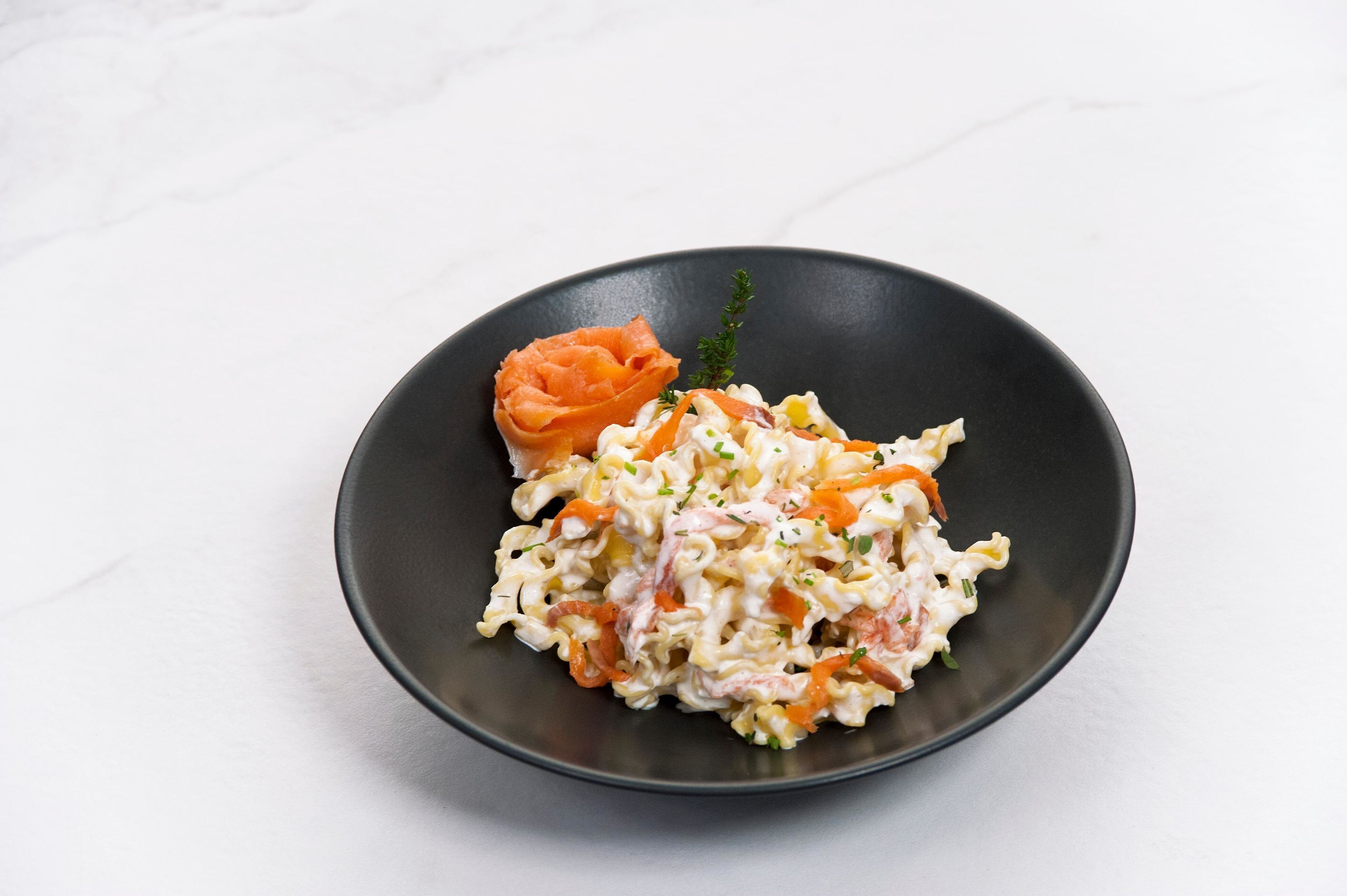 A black plate with a salad and smoked salmon on a white surface.