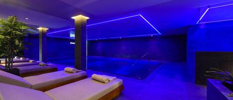 A modern spa area with massage chairs, a pool, and ambient blue lighting.