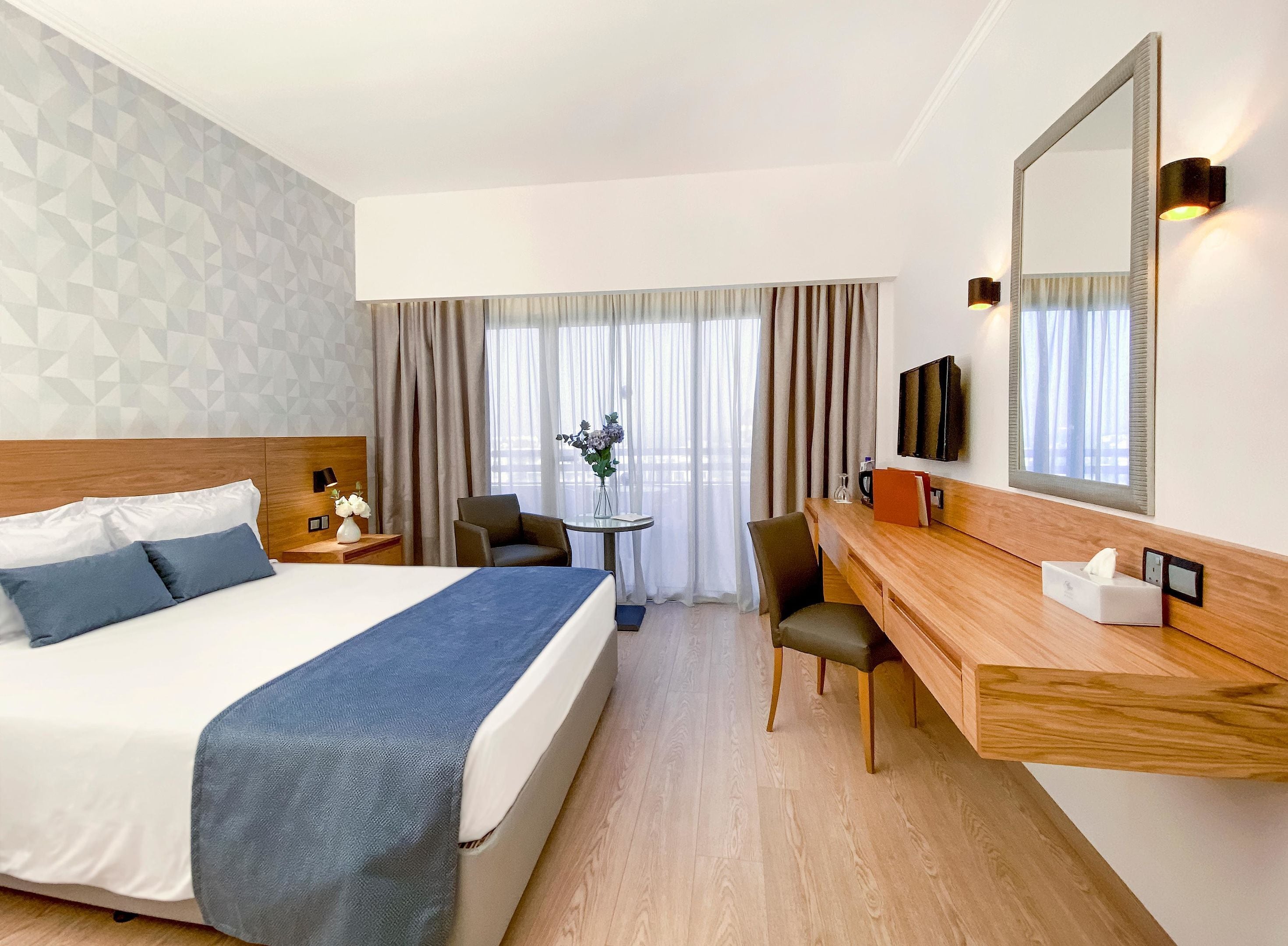 A hotel room with a bed, a desk, a chair, a TV, and a window with curtains.