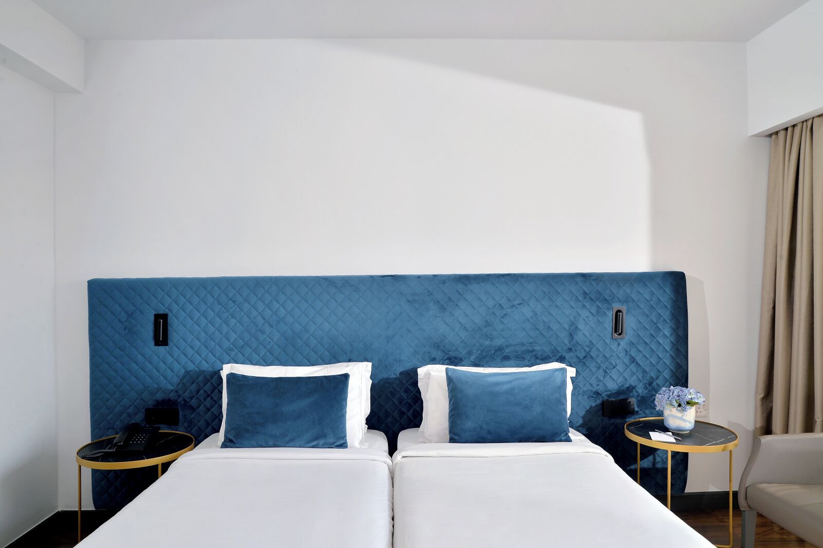 Habitación de hotel con una cama grande, dos mesitas de noche y una pequeña mesa con un florero.