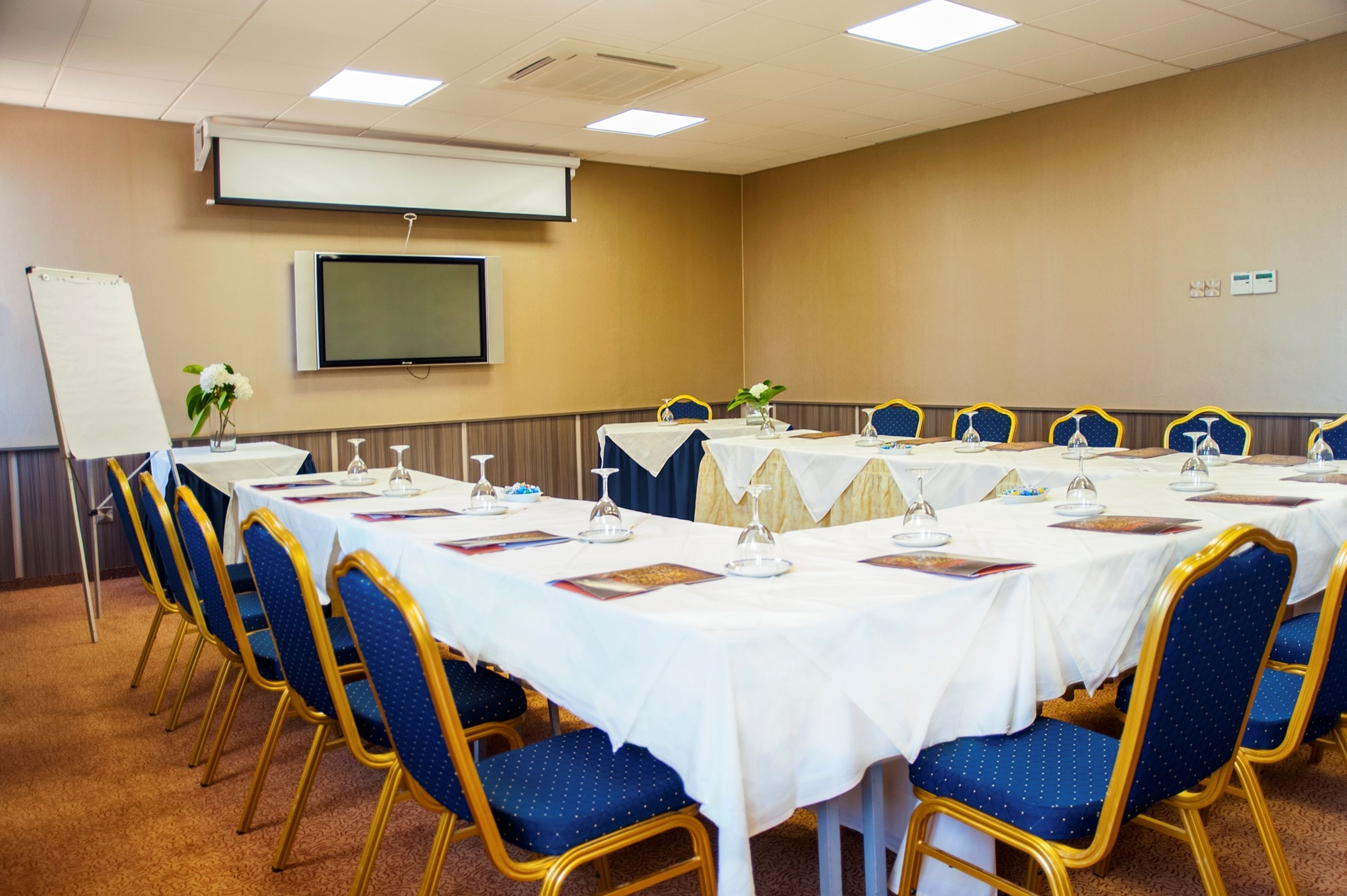 A conference room with a long table, blue chairs, and a projector screen.