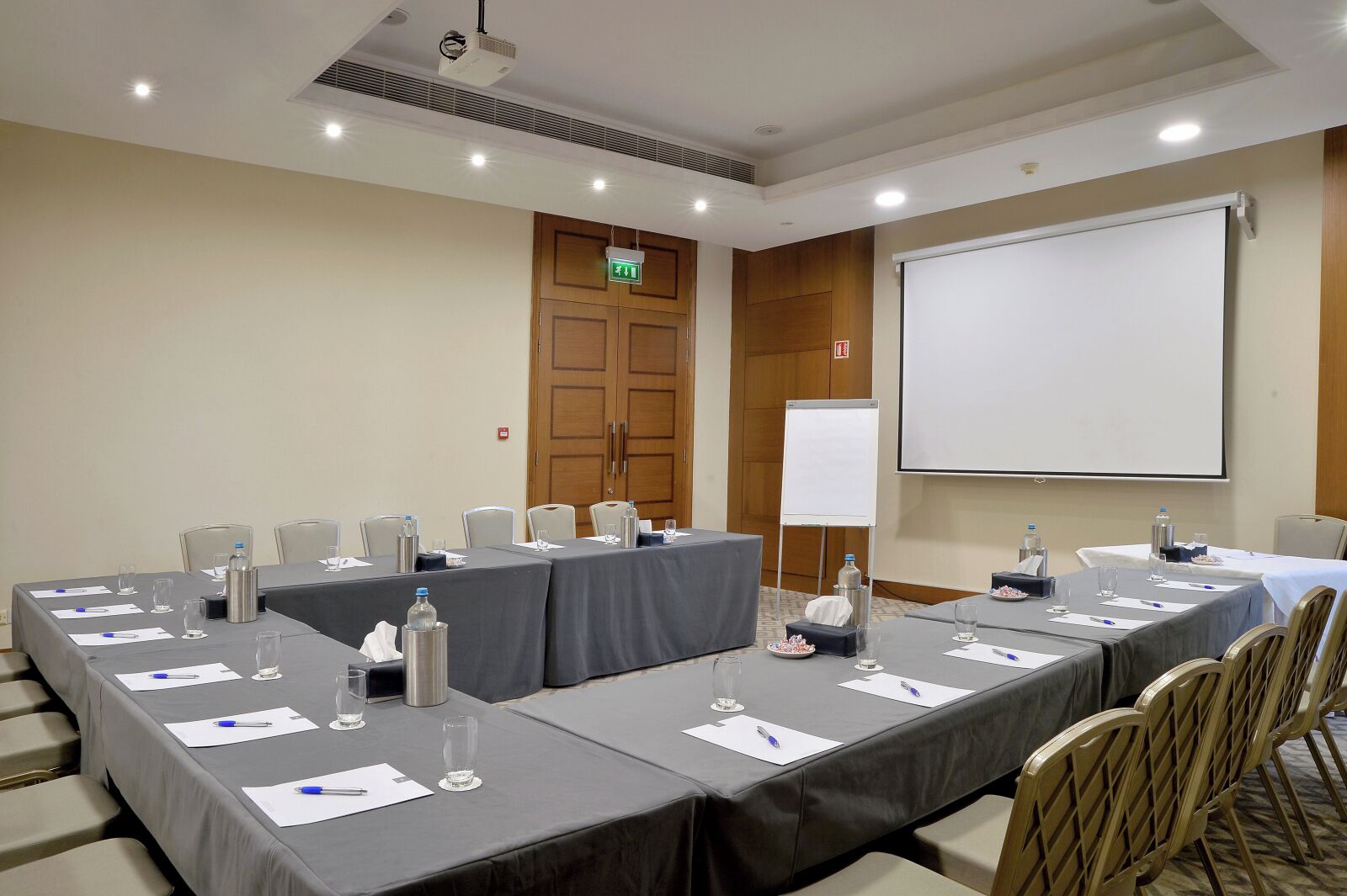 A conference room with long tables, chairs, a projector screen, and a whiteboard.