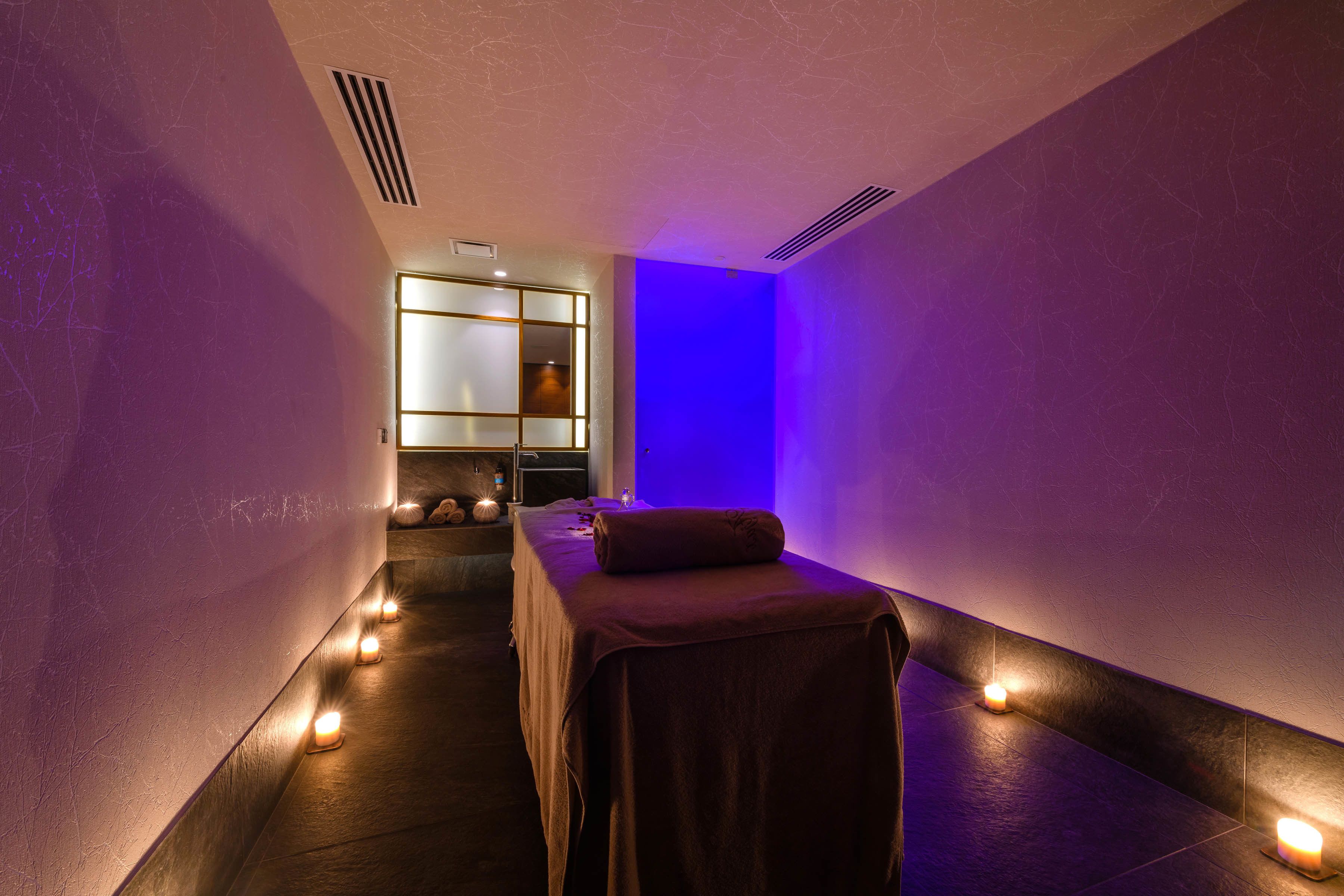 Une salle de spa équipée d’une table de massage, de bougies et d’un mur éclairé en bleu.