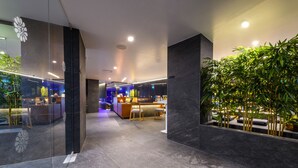 A modern hotel lobby with a reception desk, seating area, and a large indoor plant. - Ajax Hotel (Limassol)