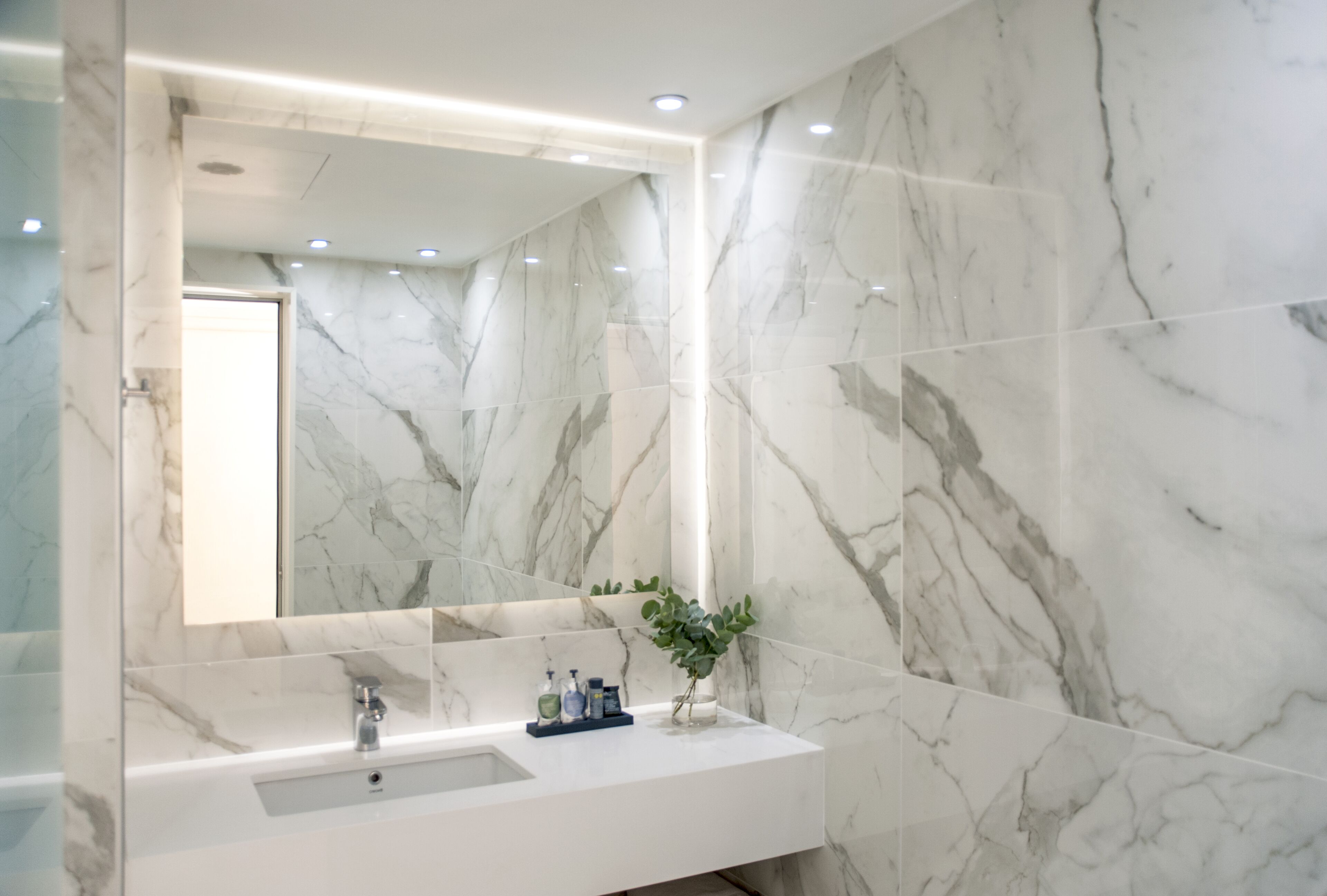 A modern bathroom with a marble backsplash, a large mirror, and a white sink.