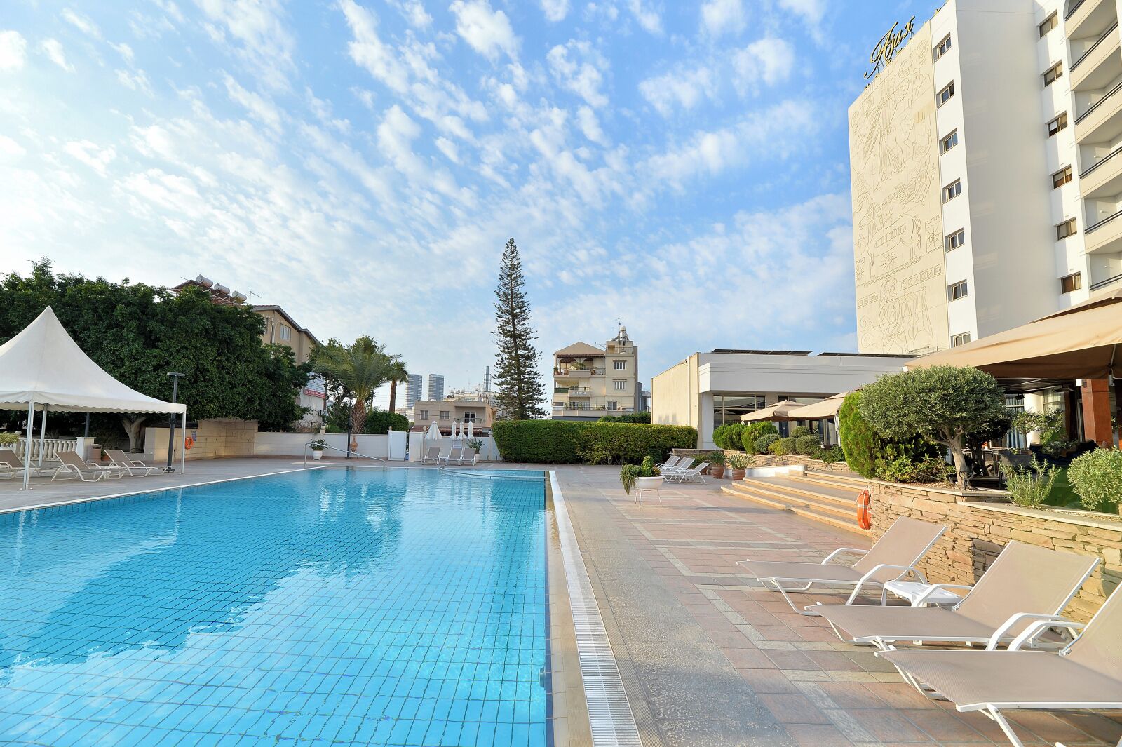 A swimming pool with lounge chairs, a white tent, and a building with a mural.