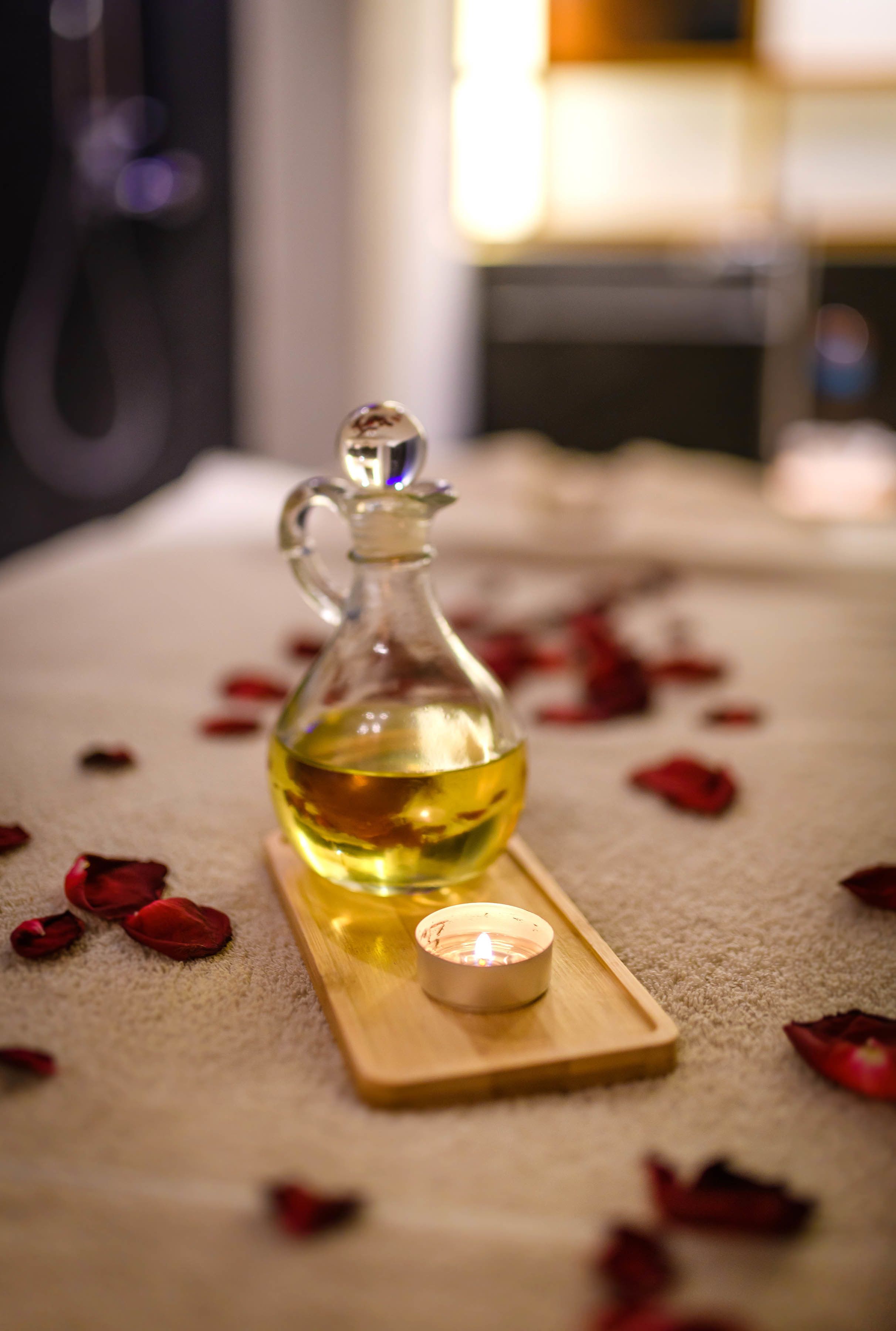 A candle and a bottle of oil on a wooden tray.
