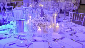 A banquet hall with round tables set for a formal event, featuring white linens, glassware, and floral centerpieces.