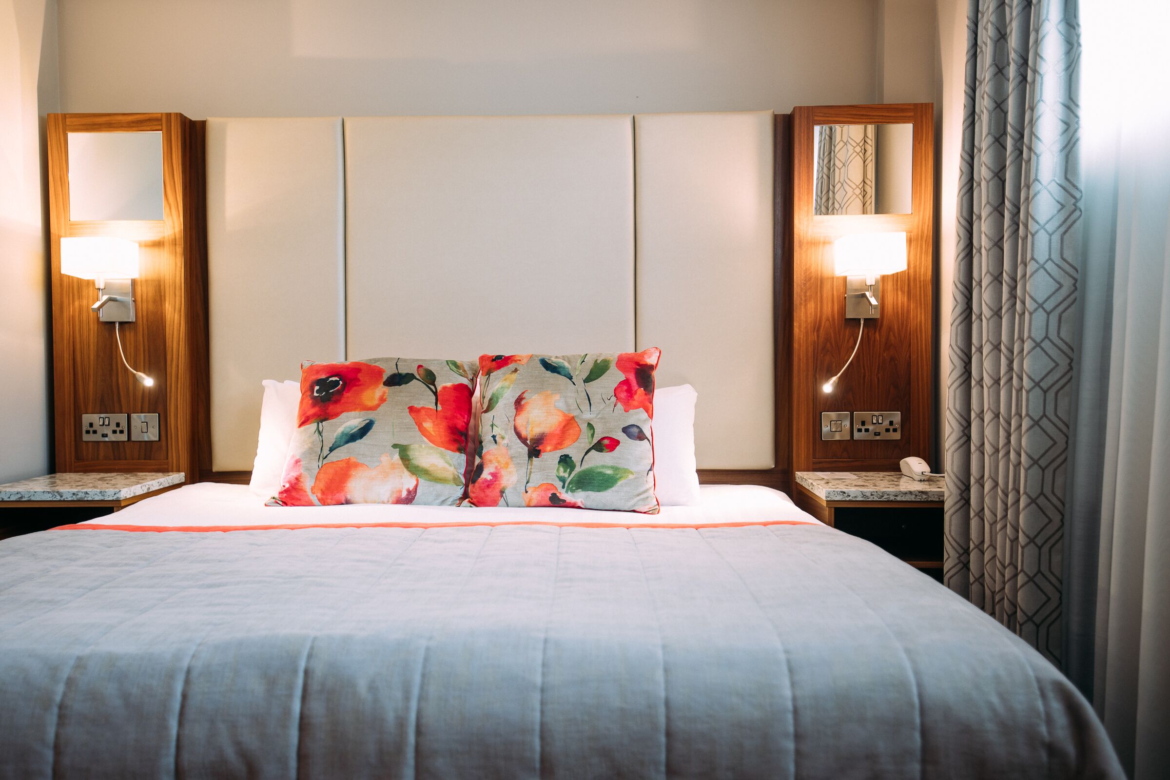 A hotel room with a large bed, two bedside lamps, a nightstand, and a mirror.