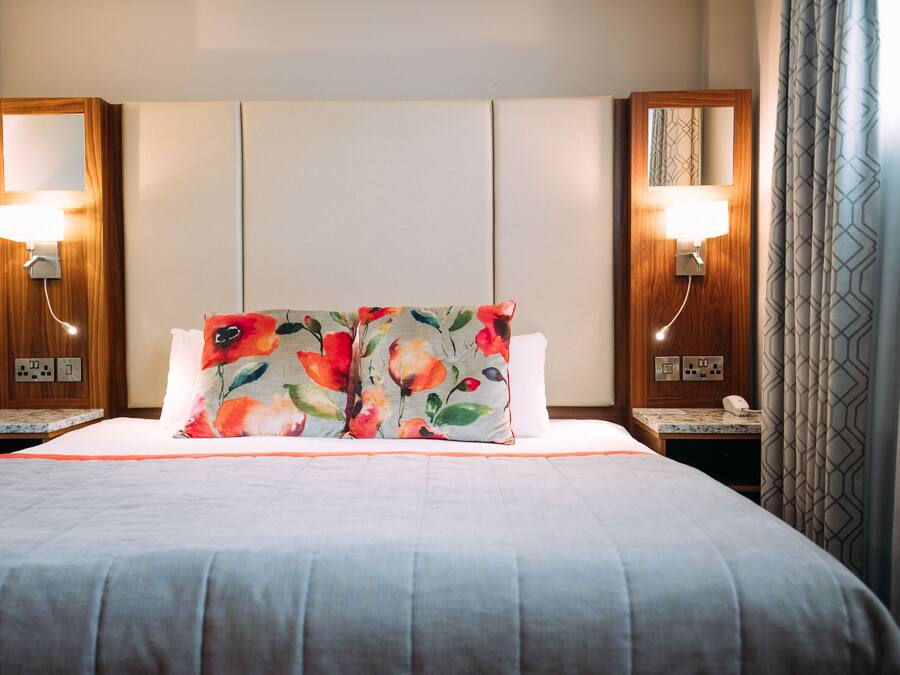 A hotel room with a large bed, two bedside lamps, a nightstand, and a mirror.