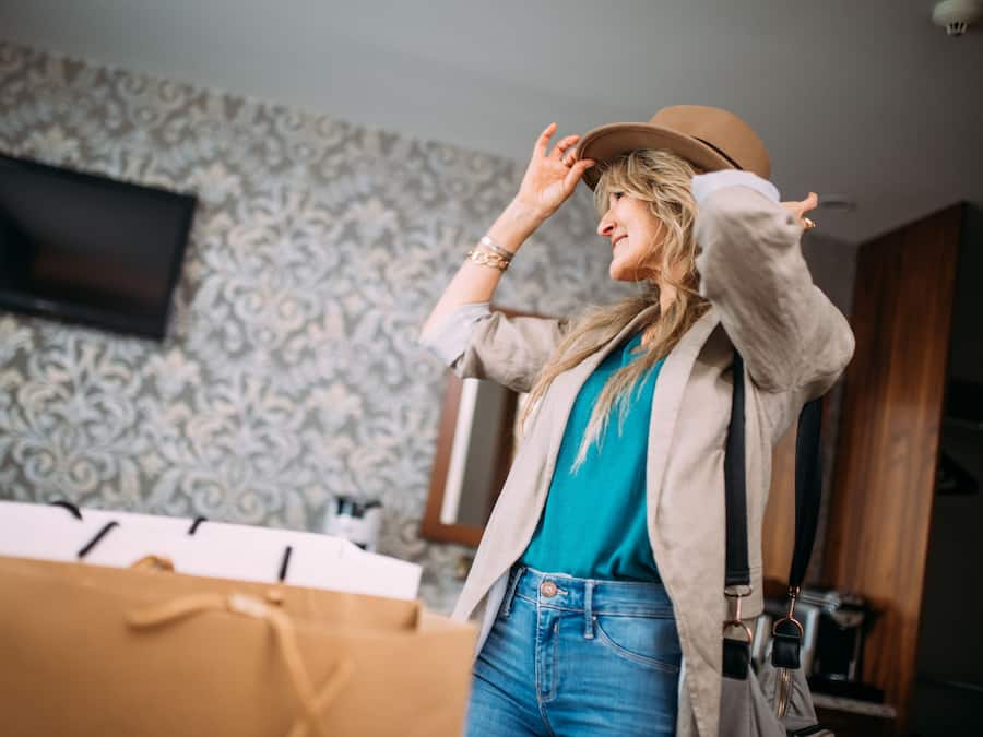 A room with patterned wallpaper, a flat-screen TV mounted on the wall, and a large brown shopping bag on the floor.