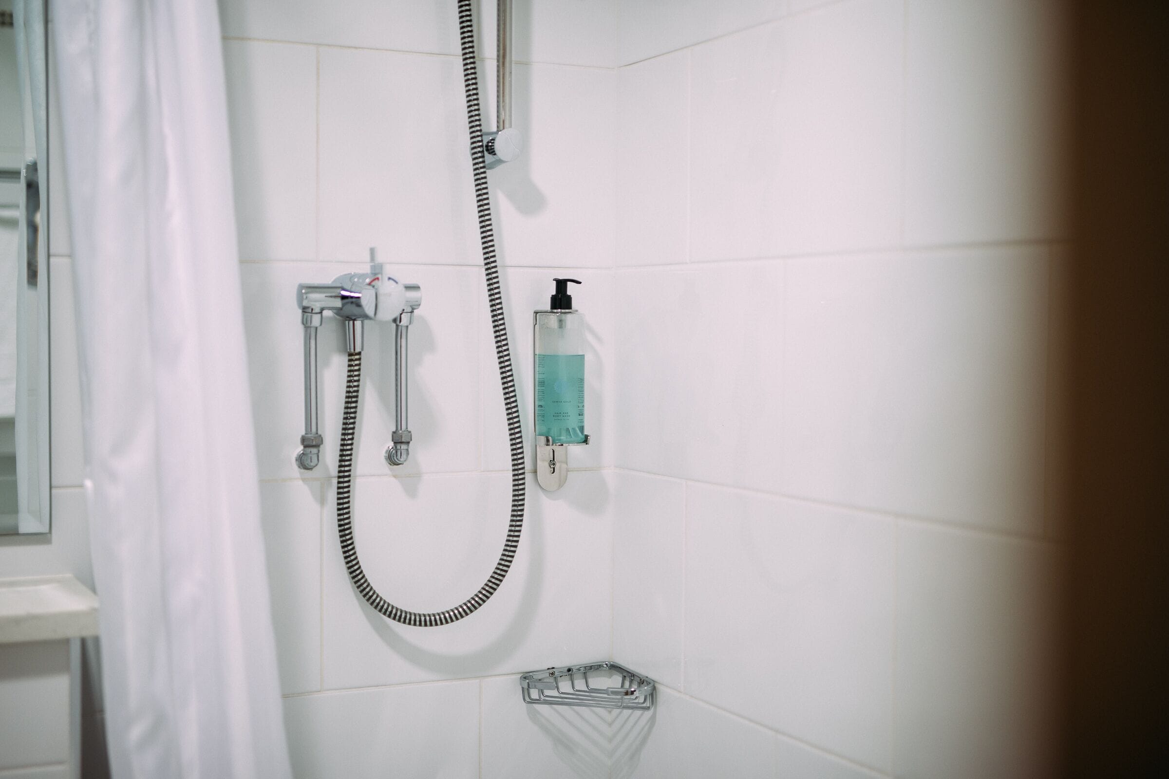 A shower with a handheld showerhead, a wall-mounted faucet, and a soap dispenser.