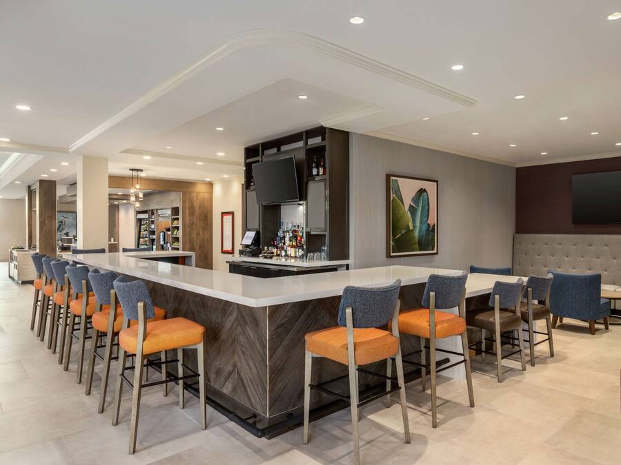 A modern bar area with a long counter, multiple bar stools, and a television mounted on the wall.