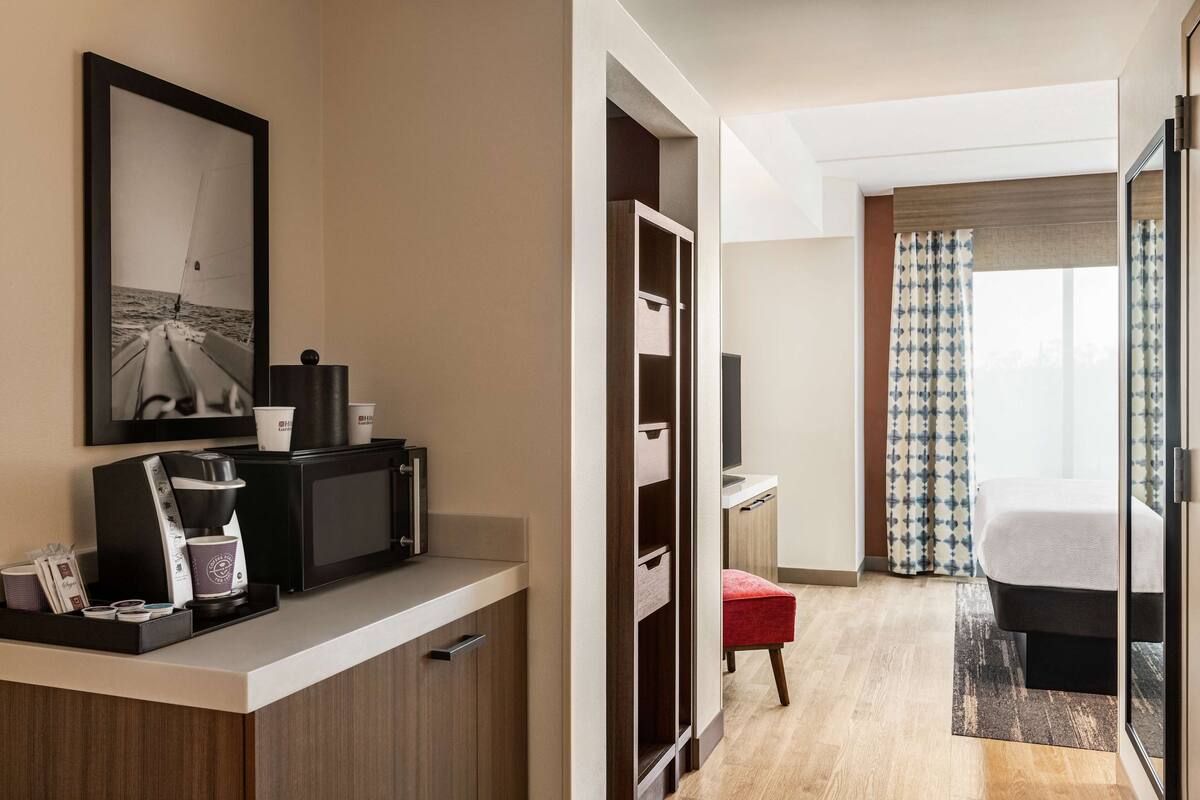 Een hotelkamer met een kitchenette, een bed, een televisie en een raam met gordijnen.
