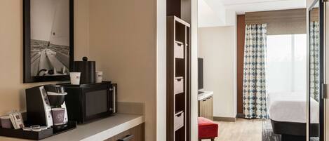 Habitación de hotel con kitchenette, una cama, televisor y ventana con cortinas.