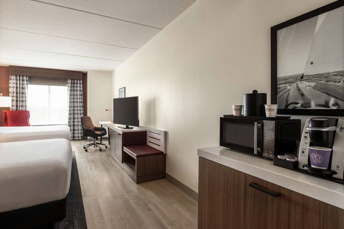 Een hotelkamer met twee bedden, een bureau met een televisie, een koffiezetapparaat en een lijst aan de muur.