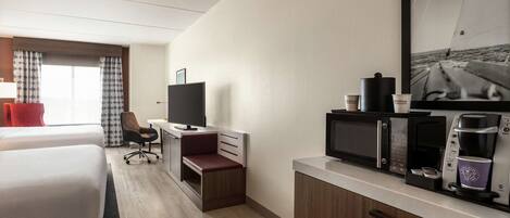A hotel room with two beds, a desk with a TV, a coffee maker, and a framed picture on the wall.