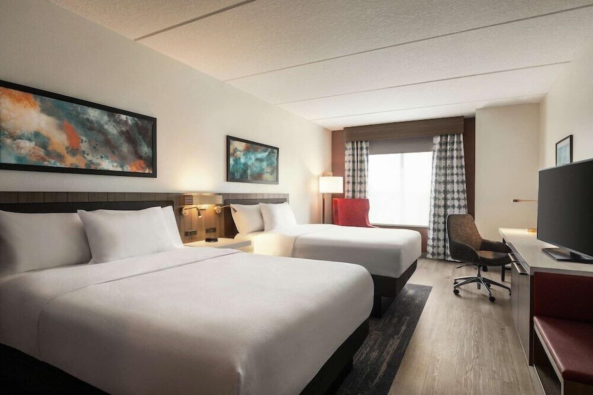 Een hotelkamer met twee bedden, een bureau met stoel, een televisie en kunstwerken aan de muren.