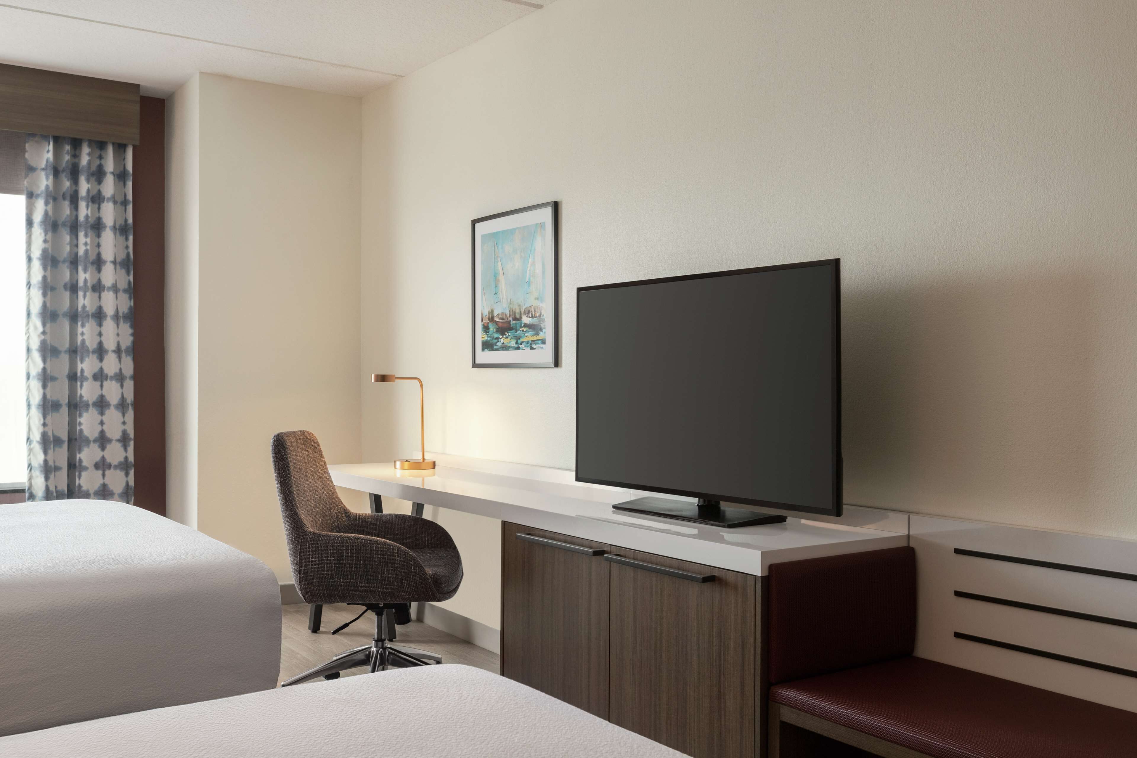 Ein Hotelzimmer mit zwei Betten, einem Schreibtisch mit Fernseher und einem Sessel.
