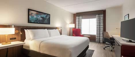 A hotel room with a large bed, a desk with a chair, a television, and a red armchair.