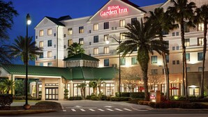 Ein mehrstöckiges Hotel mit einem gut sichtbaren Schild "Hilton Garden Inn", einem Eingang mit Gründach und Palmen im Vordergrund.