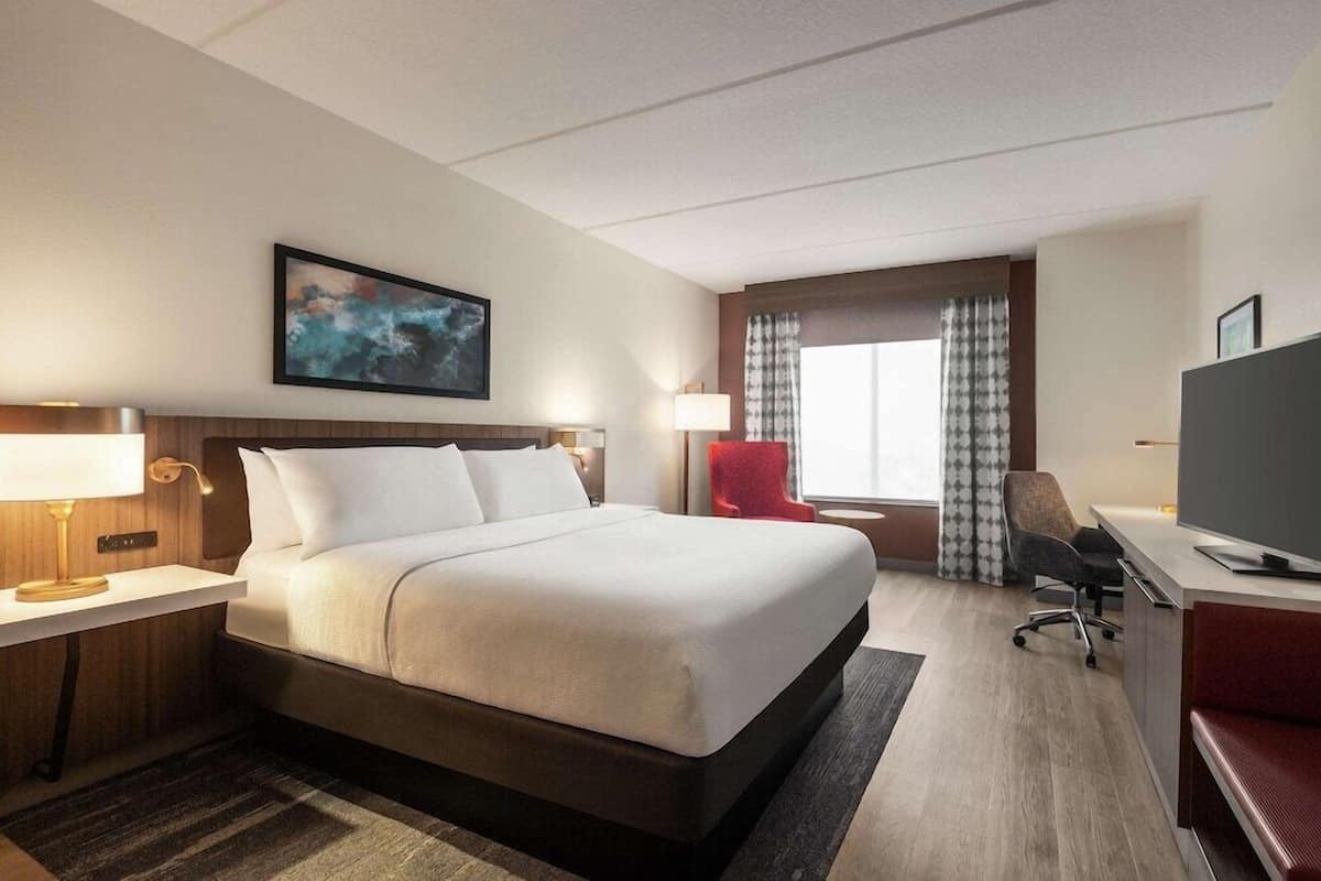 Een hotelkamer met een groot bed, een bureau met stoel, een televisie en een raam met gordijnen.