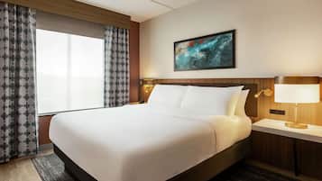 A hotel room with a large bed, a nightstand with a lamp, a painting on the wall, and a window with curtains.