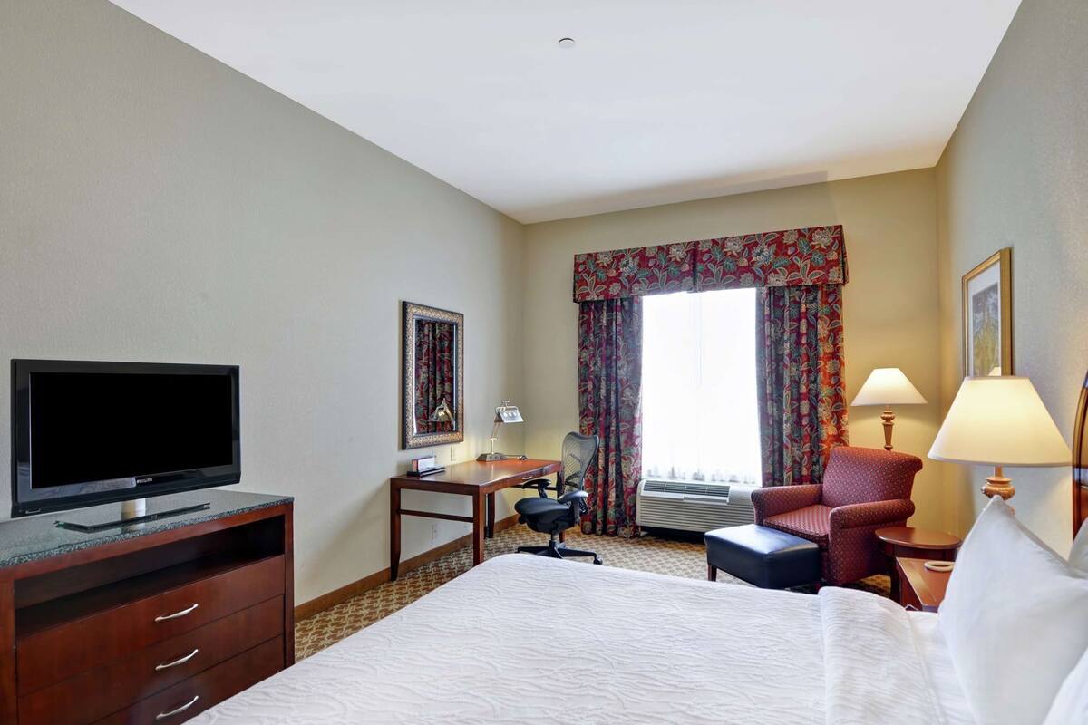 A hotel room with a bed, a desk, a chair, a television, and a window with curtains.