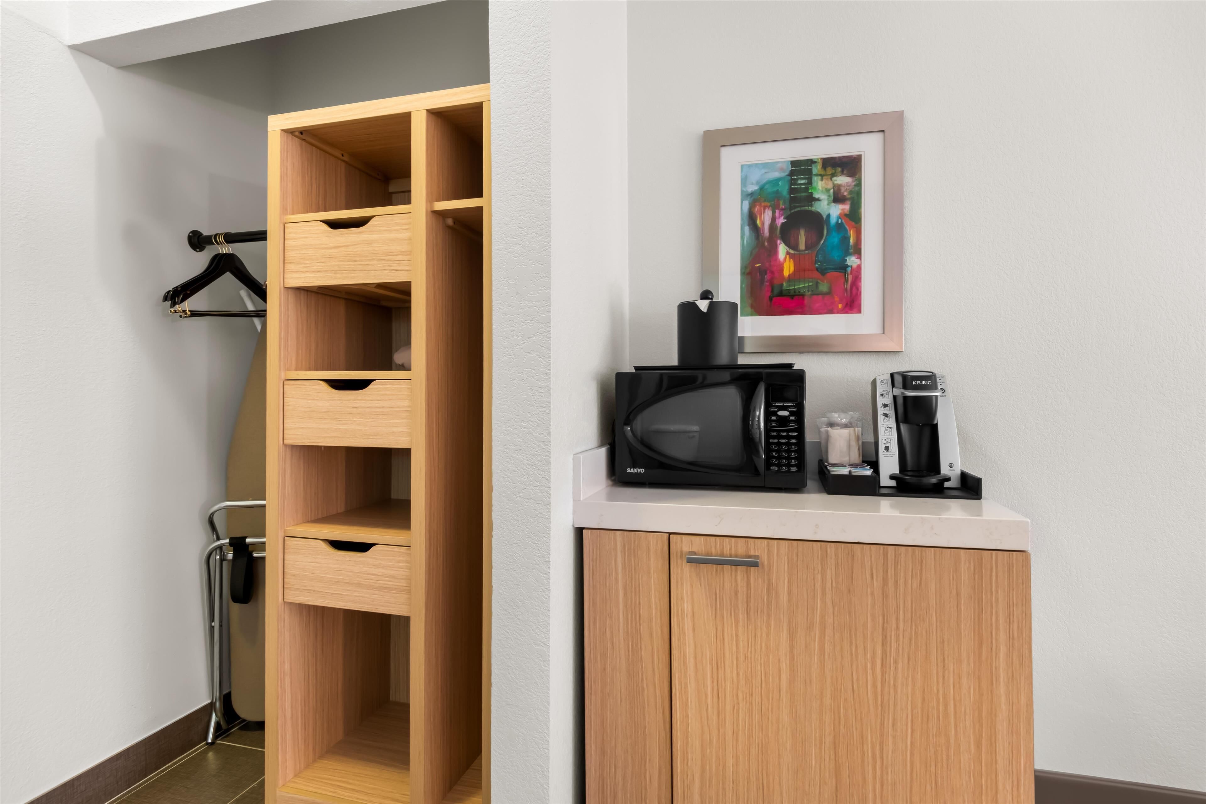 Een kitchenette met een magnetron, koffiezetapparaat en een schilderij boven de aanrecht.