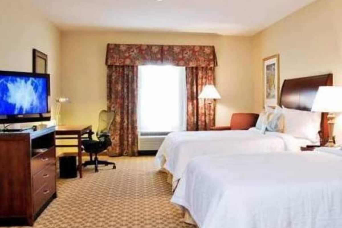 A hotel room with two beds, a desk, a chair, a television, and a window with curtains.