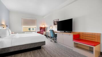 Una habitación de hotel moderna con cama, escritorio, silla, televisor y zona de estar.