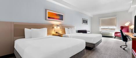 A hotel room with two beds, a desk, a chair, a lamp, a painting, and a window with blinds.