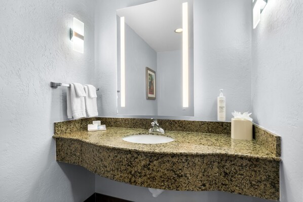 A bathroom with a granite countertop, a white sink, and a large mirror.