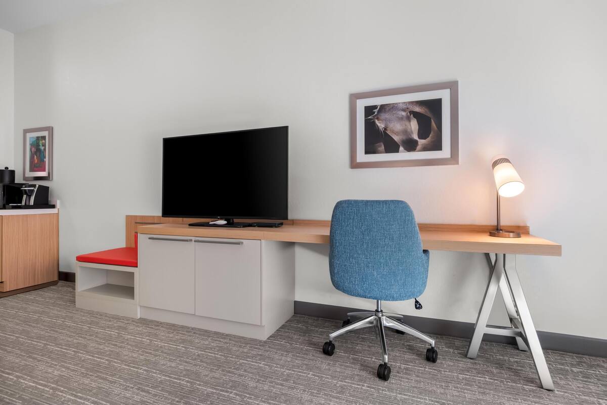 A modern office space with a desk, chair, TV, lamp, and framed picture on the wall.