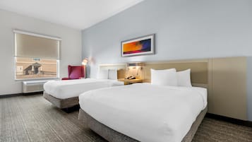 Una habitación de hotel con dos camas, una silla roja, una mesita de noche con lámpara, un cuadro en la pared y una ventana con persianas.
