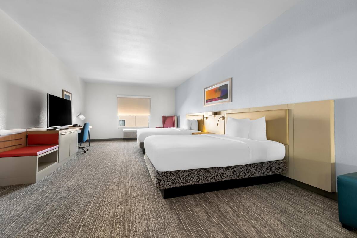 A hotel room with a bed, a desk, a TV, and a window.
