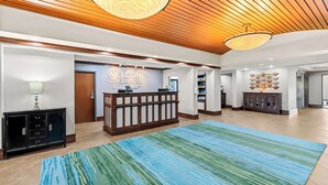 A reception area with a wooden ceiling, a reception desk, a welcome sign, a blue striped rug, and a cabinet with glass doors. - Hampton Inn Chattanooga - North/Ooltewah (Ooltewah)