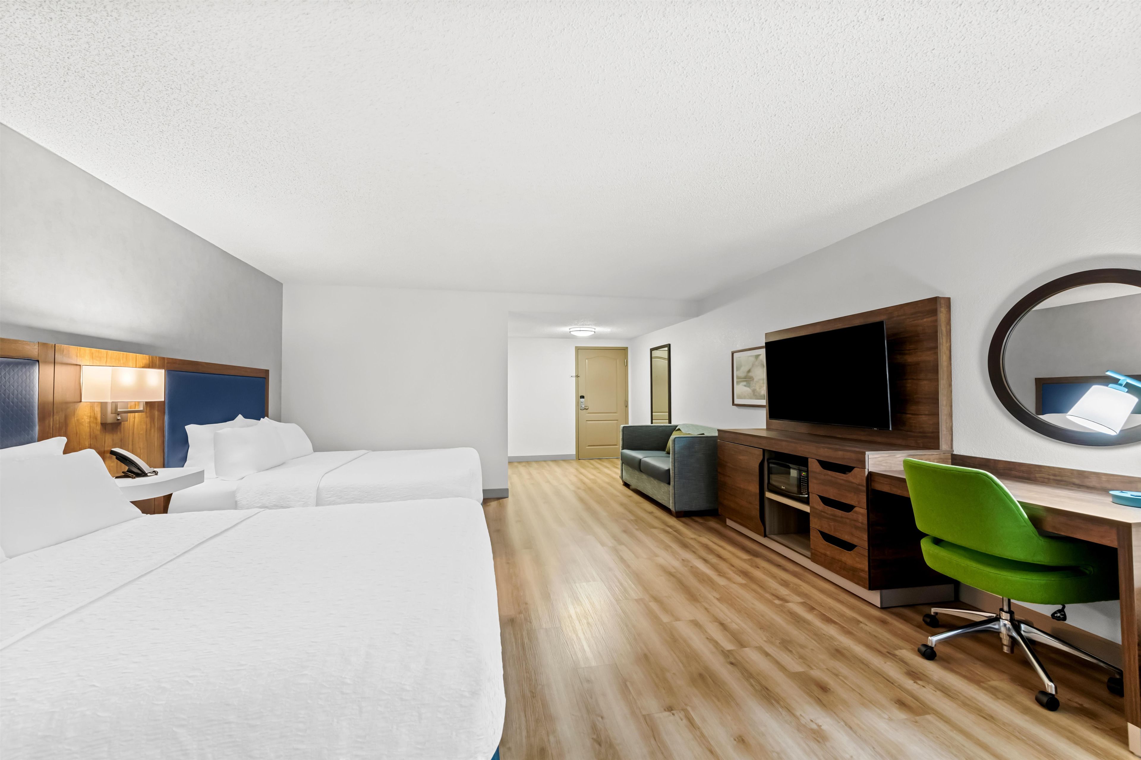 Una habitación de hotel con cama, escritorio, silla, televisor y espejo.