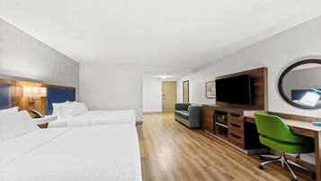 A hotel room with two beds, a desk with a chair, a TV, a mirror, and a door leading to another room.