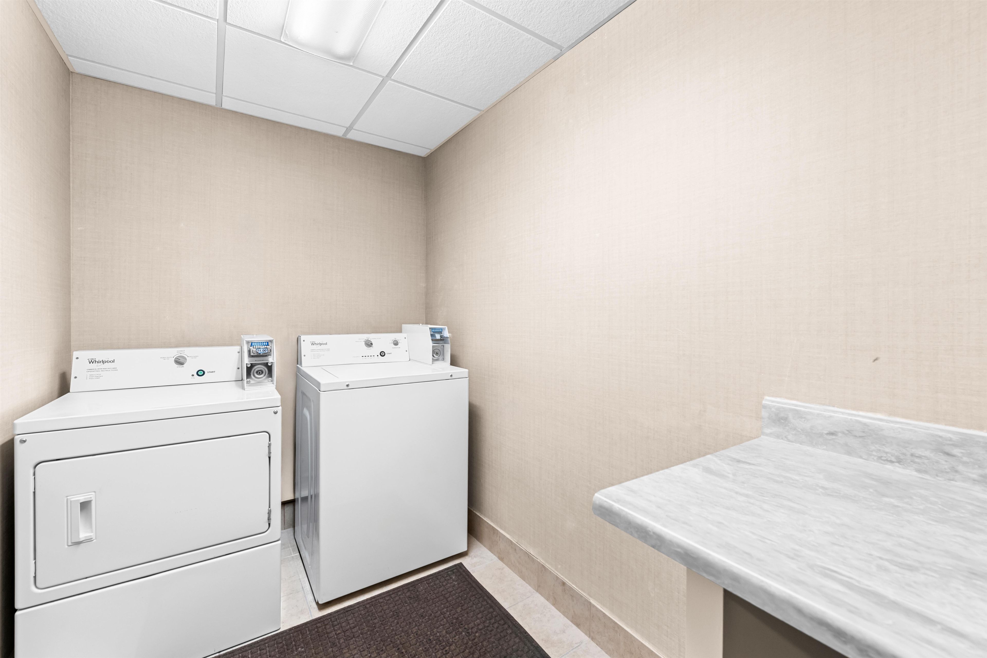 A laundry room with two stacked washers and dryers, a marble countertop, and a textured wall.