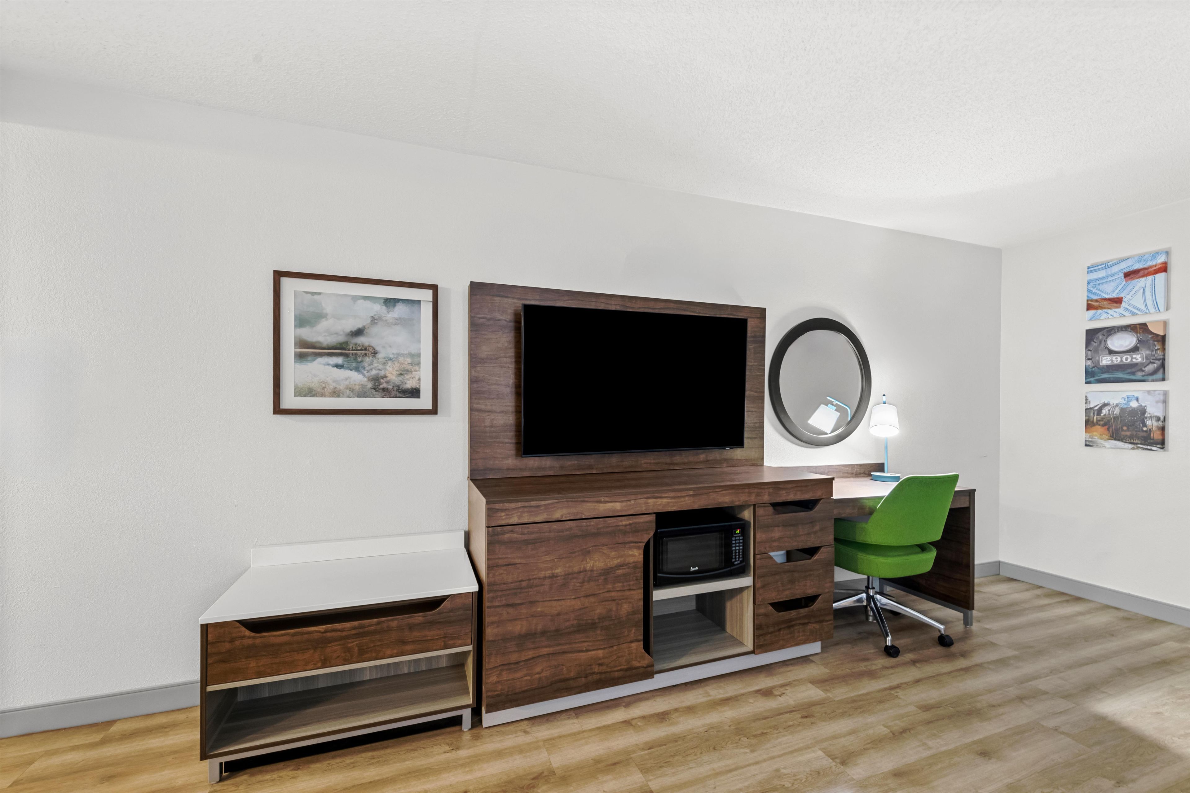Ein modernes Schlafzimmer mit Schreibtisch aus Holz, einem Flachbildfernseher, einem Spiegel und einem grünen Stuhl.