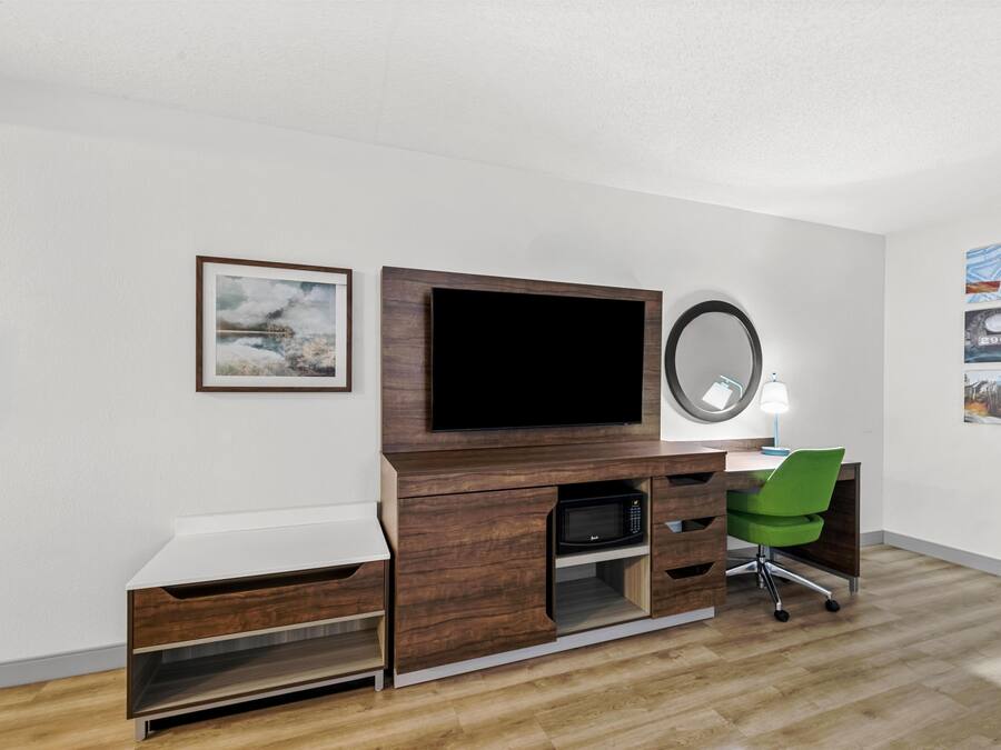 Ein modernes Schlafzimmer mit Schreibtisch aus Holz, einem Flachbildfernseher, einem Spiegel und einem grünen Stuhl.
