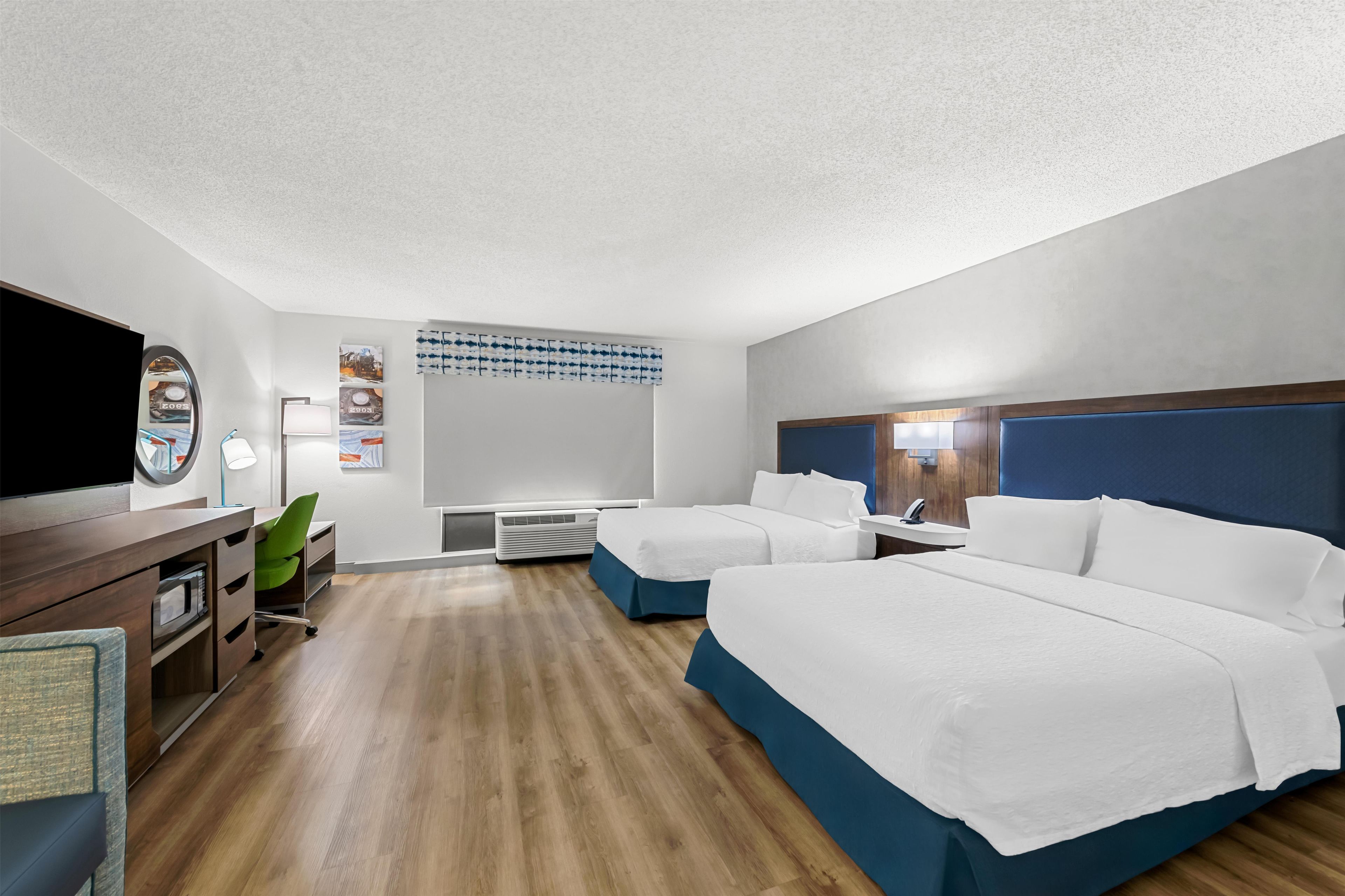 A hotel room with two beds, a desk, a chair, and a television.