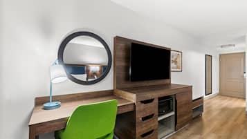 Una habitación moderna con un escritorio de madera, una silla verde, un espejo redondo, un televisor de pantalla plana y un mueble empotrado para entretenimiento.