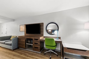 Une chambre moderne avec un bureau en bois, un téléviseur à écran plat, un fauteuil de bureau vert, un miroir rond et un canapé.