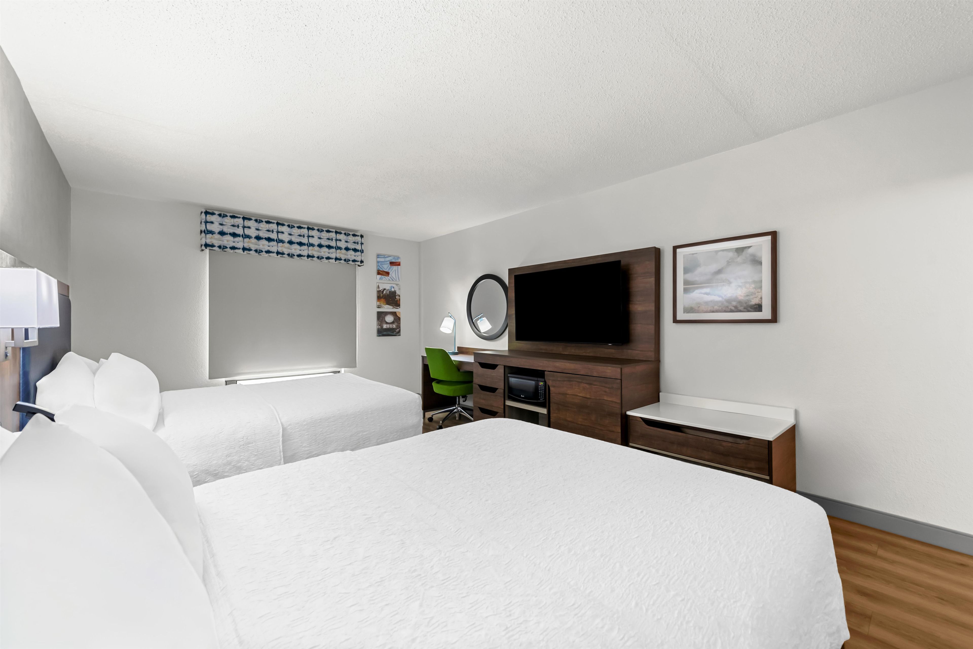 Une chambre d’hôtel avec deux lits, un bureau avec un ordinateur, un téléviseur à écran plat, un four à micro-ondes et un petit placard.