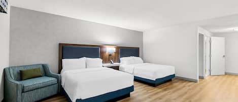 A hotel room with two beds, a sofa, a bedside table, and a door.